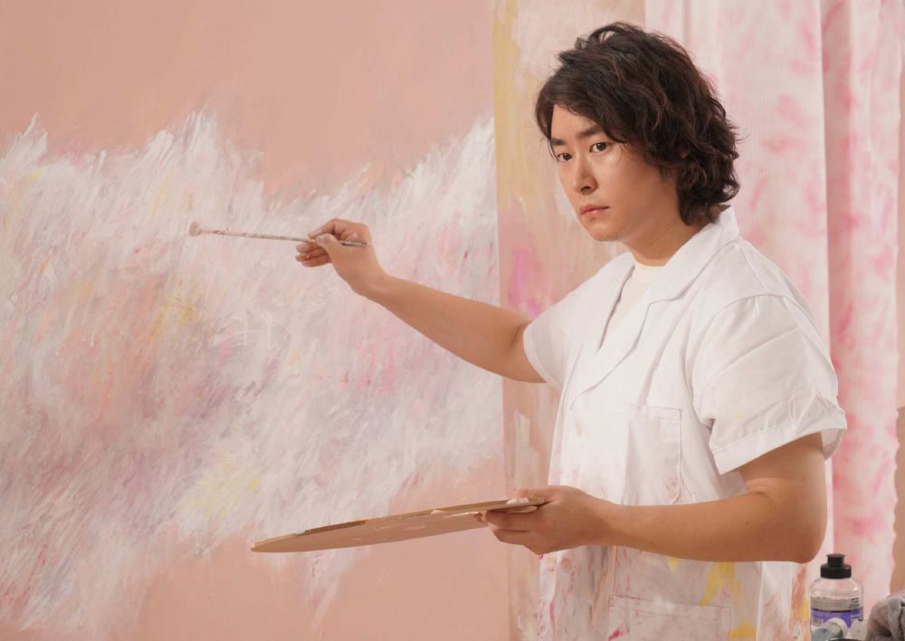 艺术家叶帆在粉色画作前手持画笔与调色板。